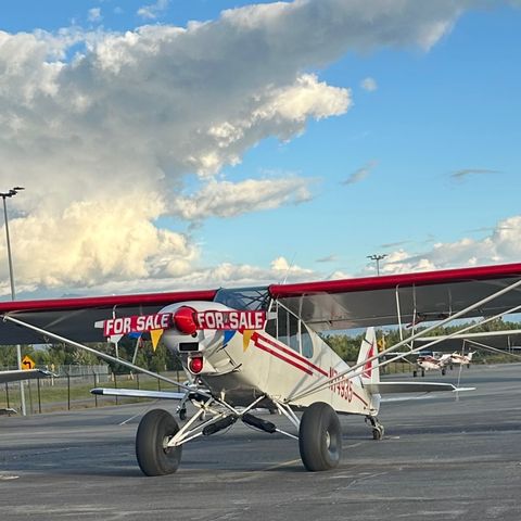 A red and white Piper PA-18 Super Cub on tundra tires, parked on an airfield ramp in Alaska.