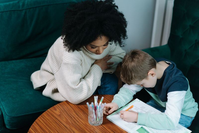 A tutor watches a boy work through a workbook on a couch.