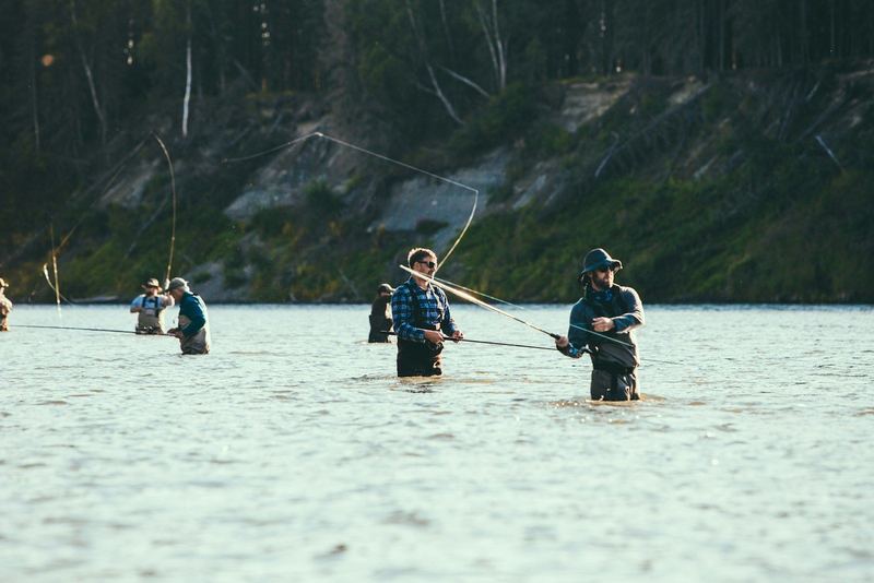 Anglers stand side by side in golden light on the Kenai River.